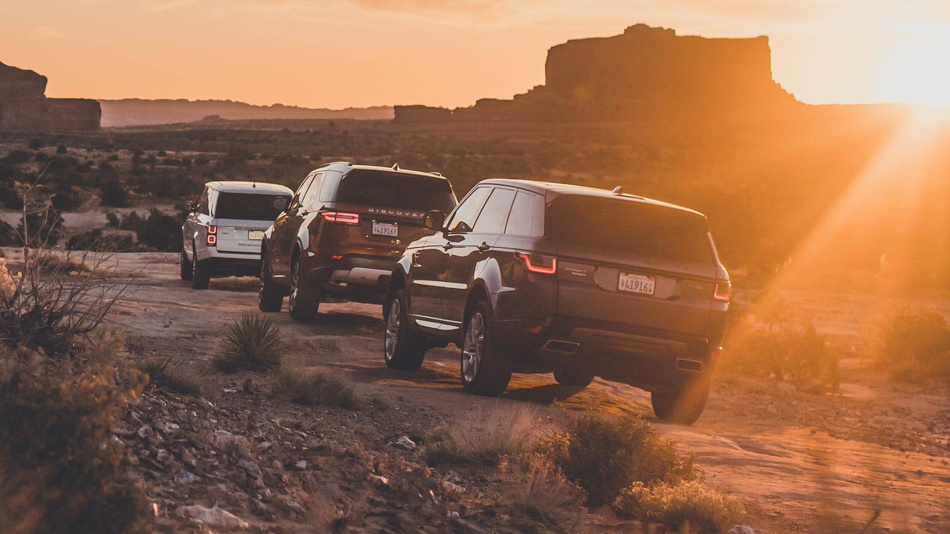 3 Land Rover vehicles driving over rocky ground as the sun sets